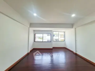 Spacious empty room with polished wooden floors and large windows offering natural light.