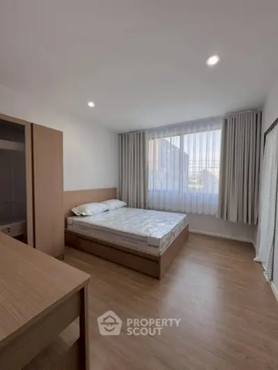 Modern bedroom with wooden flooring and large window for natural light