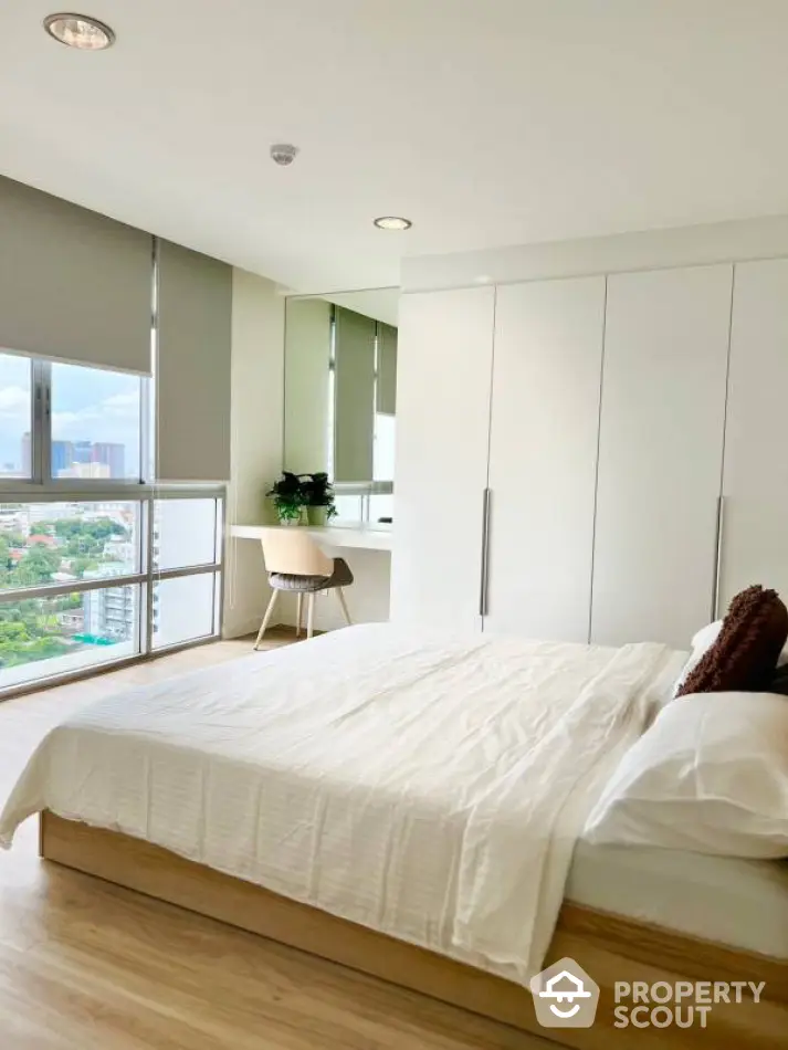 Modern bedroom with large windows and city view, featuring minimalist decor and built-in wardrobe.