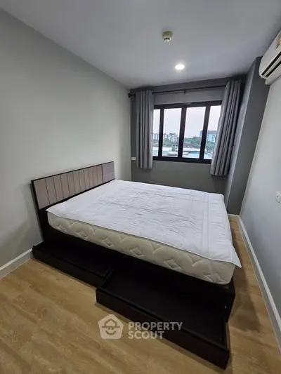 Modern bedroom with large window and wooden flooring, featuring a stylish bed and air conditioning.