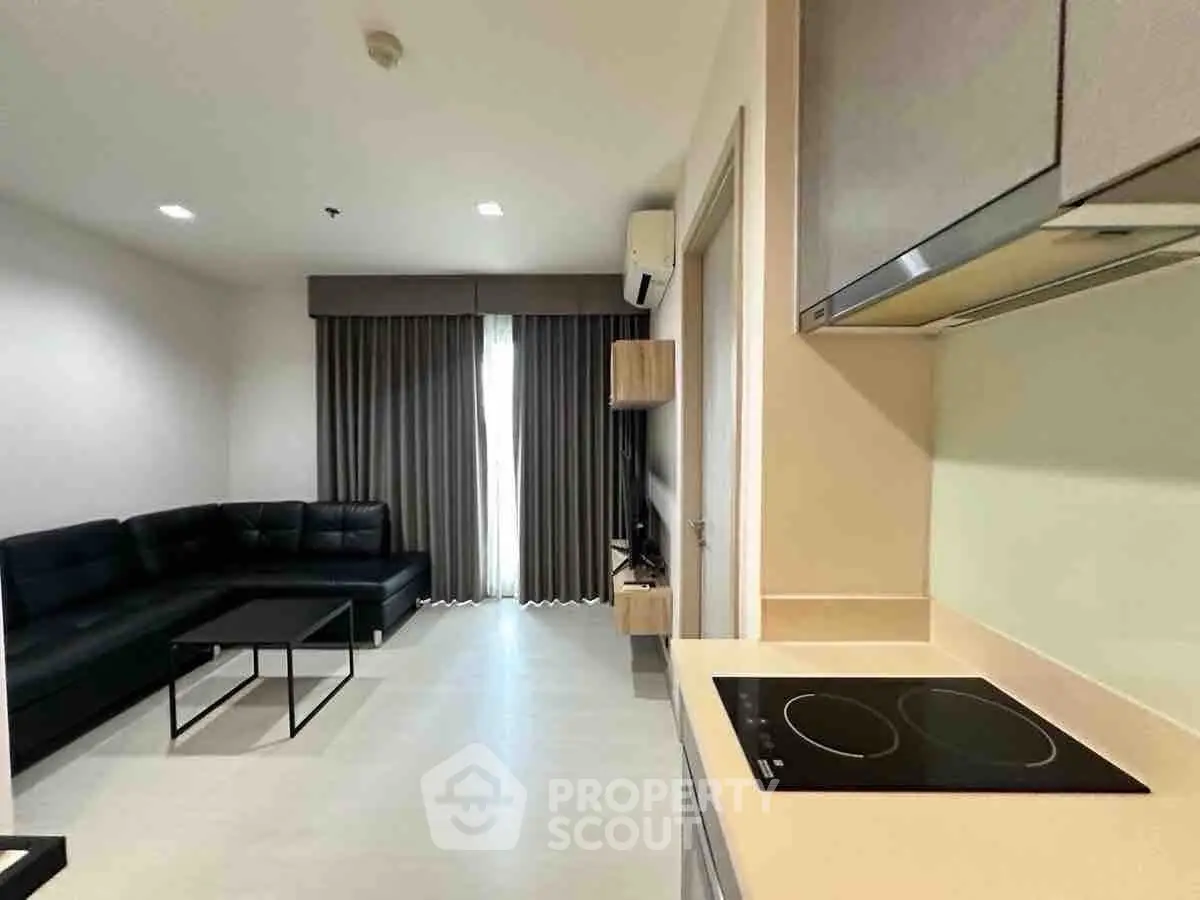 Modern living room with sleek kitchen, featuring black sofa and induction cooktop, ideal for urban living.