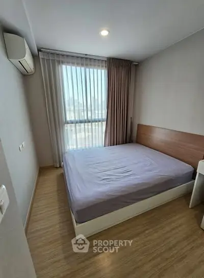 Cozy bedroom with wooden flooring and large window for natural light