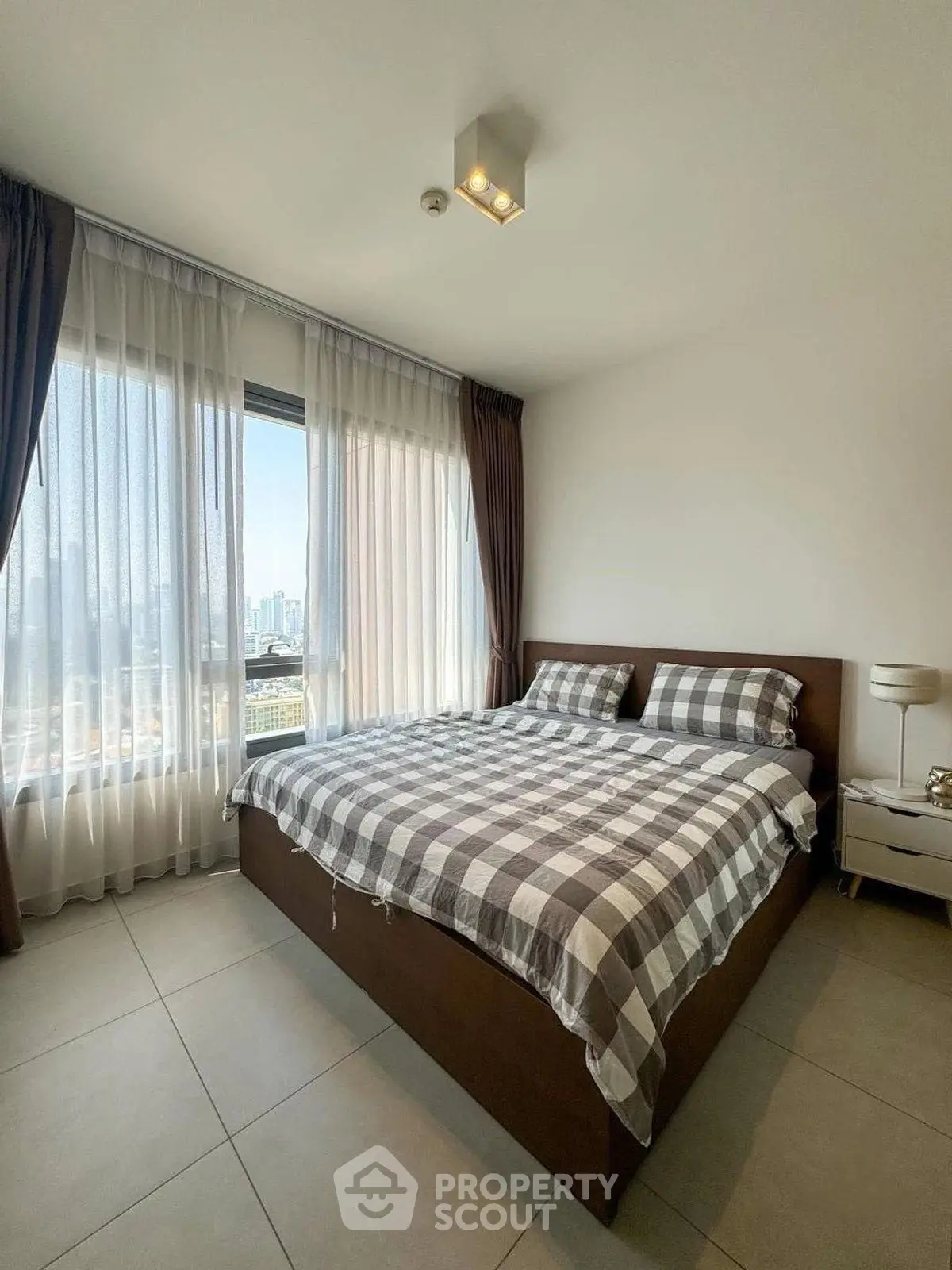 Modern bedroom with large windows and city view, featuring stylish checkered bedding.