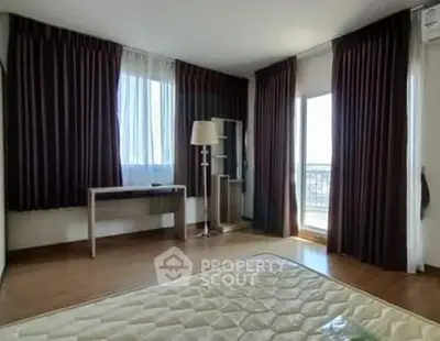 Spacious bedroom with large windows and balcony access, featuring elegant curtains and wooden flooring.