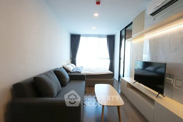Modern living room with cozy sofa, TV, and natural light from large window.