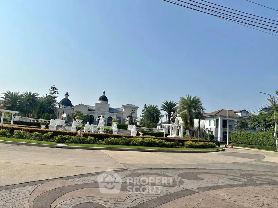 Luxurious estate entrance with elegant landscaping and grand architecture under clear blue sky.