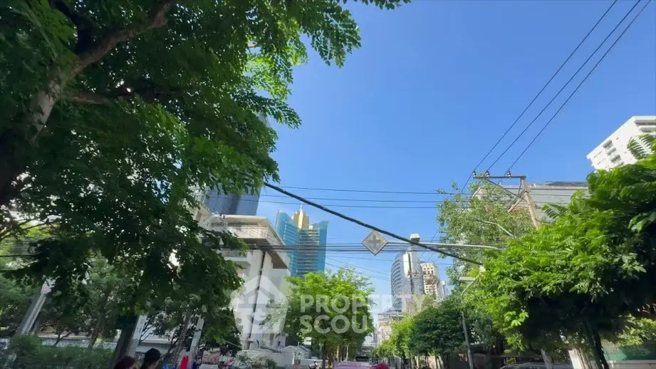 Urban street view with modern buildings and lush greenery under a clear blue sky.