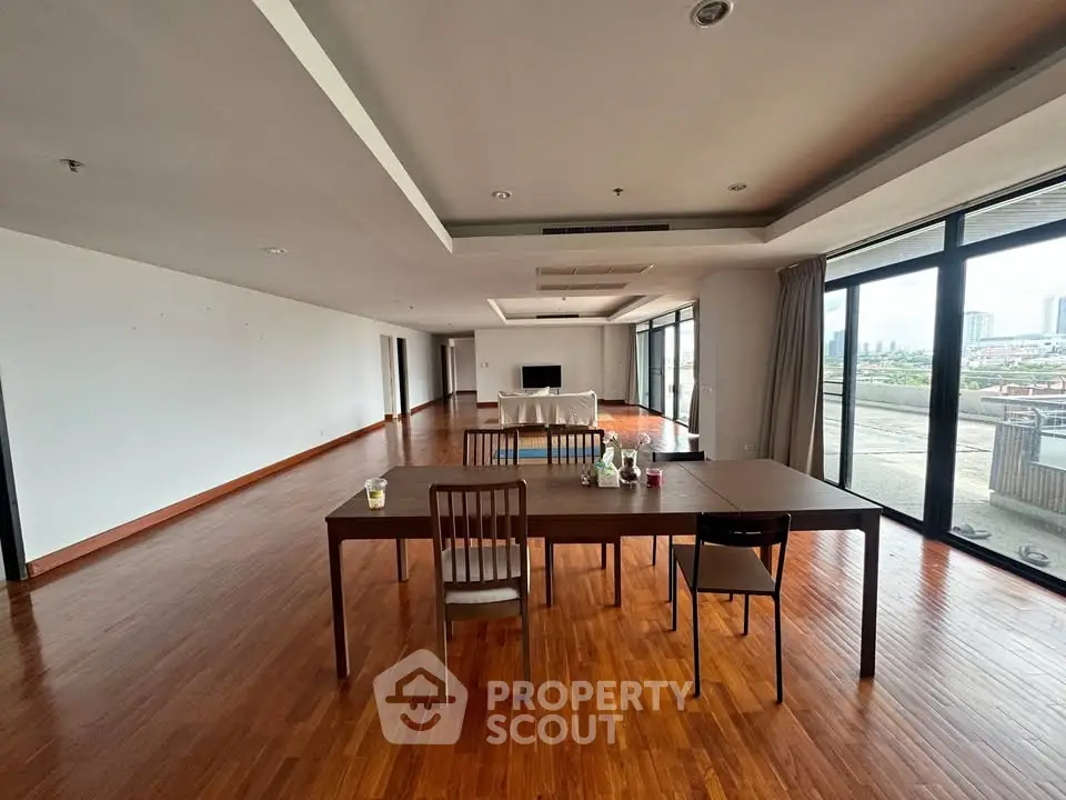 Spacious open-plan living room with hardwood floors and city view balcony.