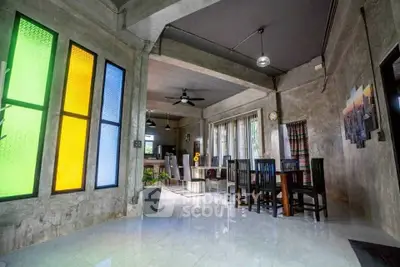 Stylish industrial-style living room with colorful stained glass windows and modern dining area.