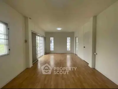 Spacious empty room with wooden flooring and large windows, perfect for customization.