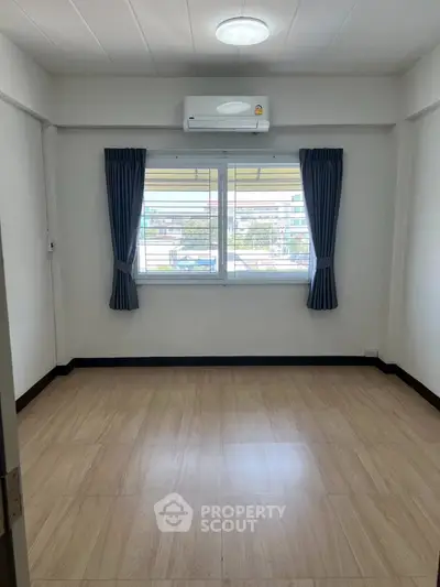 Spacious empty room with wooden flooring and large window, perfect for customization.