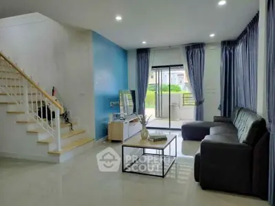 Modern living room with sleek furniture and large windows leading to a balcony.