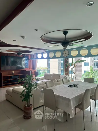 Spacious living room with modern decor and large windows offering natural light and greenery views.