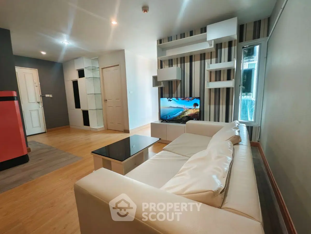 Modern living room with stylish furniture and TV, featuring a sleek white sofa and wooden flooring.