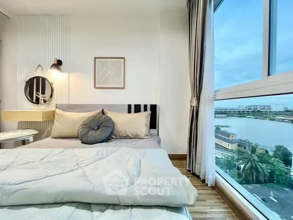 Bright bedroom with large window offering stunning river view, modern decor, and cozy bedding.