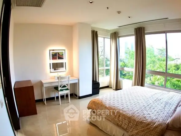 Spacious bedroom with large windows offering lush green views, featuring a cozy bed and a stylish desk area.