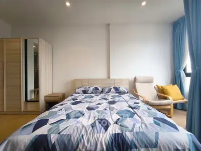 Spacious bedroom with modern decor and natural light, featuring a cozy bed and stylish chair.