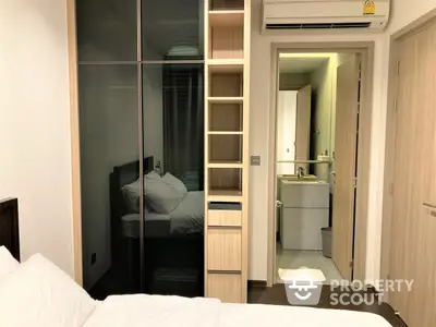 Cozy bedroom with mirrored wardrobe doors reflecting an adjacent room, leading to a well-lit ensuite bathroom, showcasing a practical and compact living space.