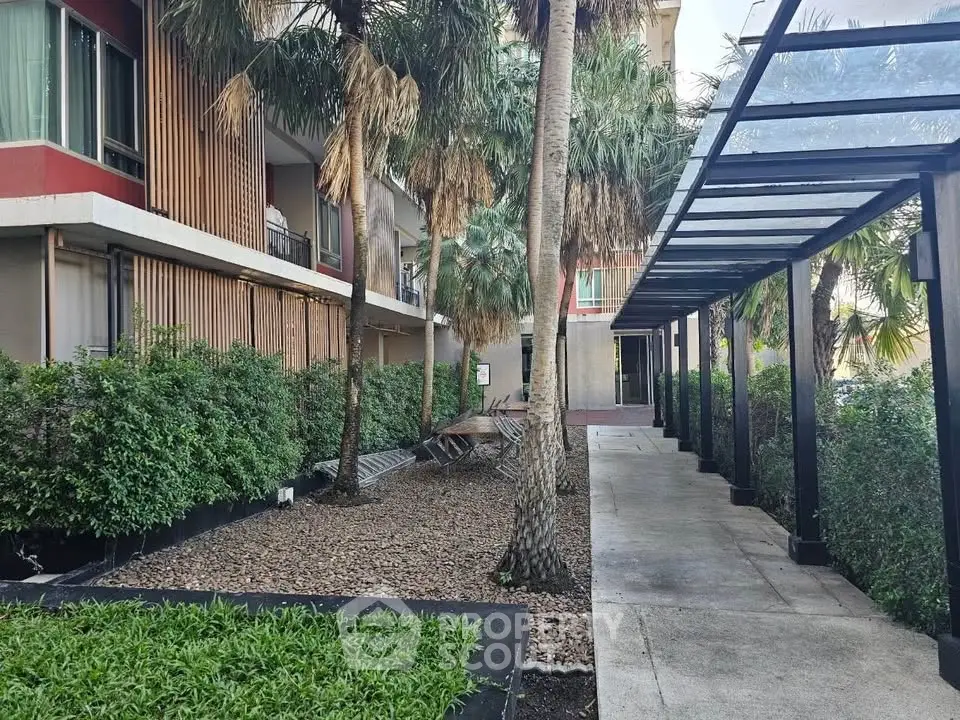 Modern apartment building with lush garden and covered walkway, offering serene urban living.
