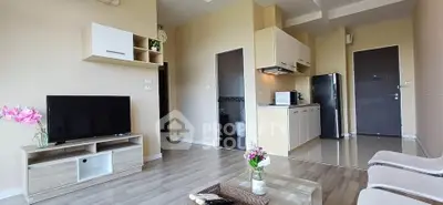 Modern living room with open kitchen, featuring sleek furniture and neutral tones.