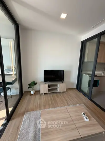 Modern living room with sleek design and natural light, featuring a TV and wooden flooring.