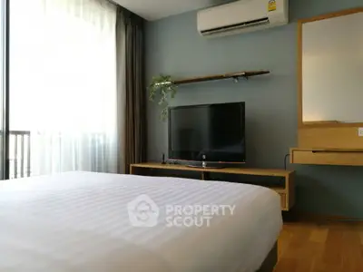 Modern bedroom with TV, air conditioning, and natural light from large window.