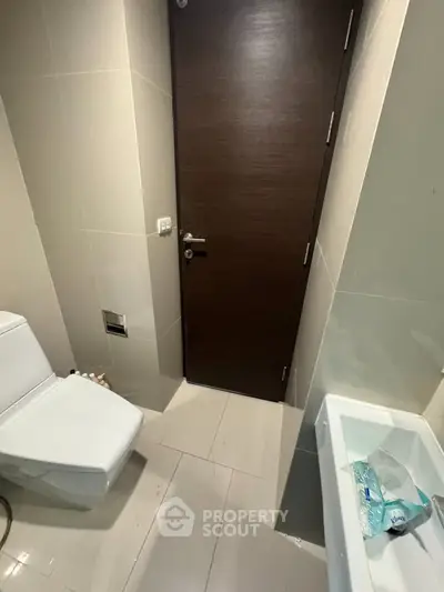 Modern bathroom with sleek fixtures and neutral tiles, featuring a toilet and sink.