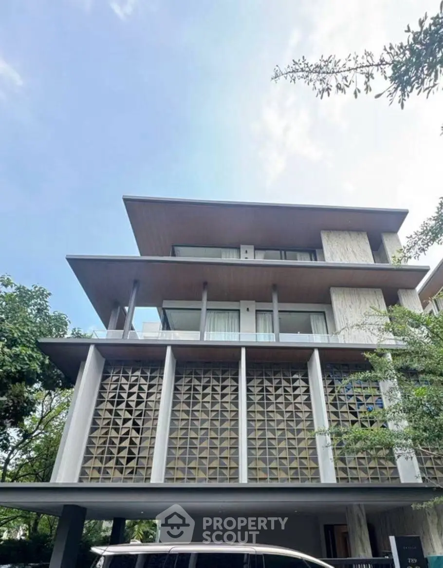 Modern multi-story building with unique facade design and lush greenery surroundings.