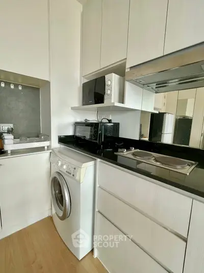 Modern compact kitchen with washing machine and microwave in sleek white cabinetry.