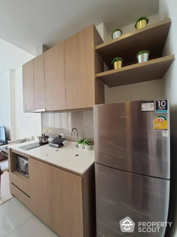 Modern kitchen with sleek wooden cabinets and stainless steel fridge in compact layout.