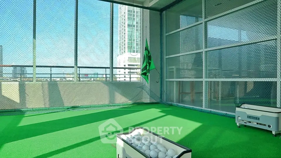 Modern indoor golf practice area with green turf and city view, perfect for sports enthusiasts.