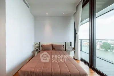 Modern bedroom with large windows and stunning river view from balcony.
