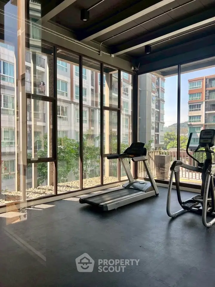 Modern gym with large windows offering a scenic view of urban buildings, featuring state-of-the-art exercise equipment.