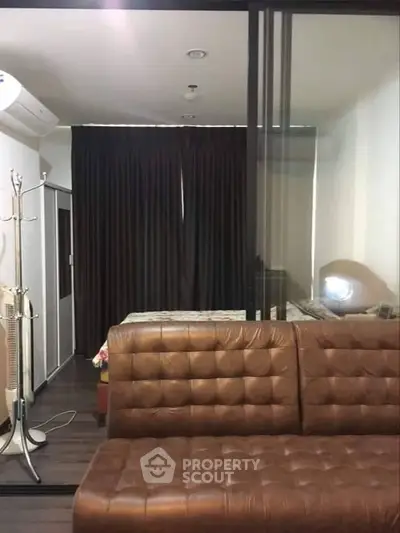 Modern studio apartment with stylish brown leather sofa and cozy bedroom area.