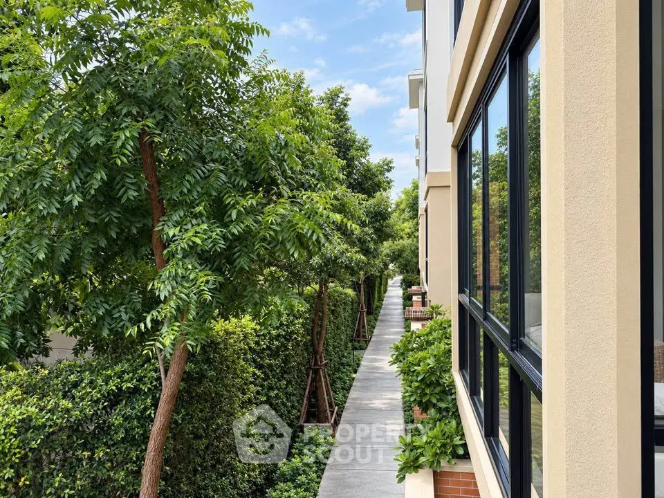 Modern building exterior with lush greenery and walkway, perfect for serene living.