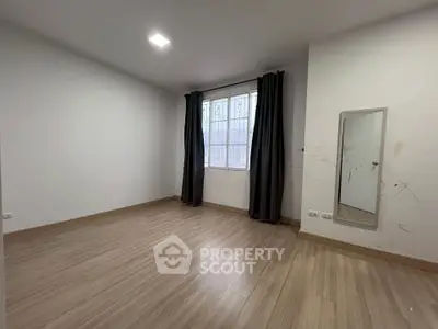 Spacious empty room with wooden flooring and large window, ideal for customization.