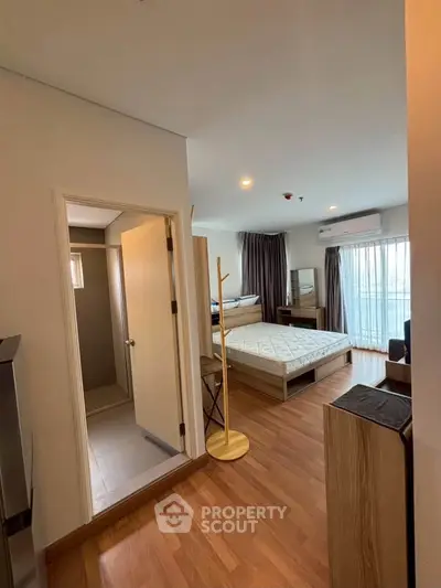 Modern studio apartment with wooden flooring, cozy bedroom, and natural light from large windows.