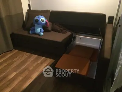 Cozy living room with brown sofa and hidden storage, featuring wooden flooring and plush toy decor.