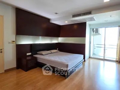 Spacious modern bedroom with balcony access and sleek wooden flooring.
