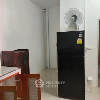Modern kitchen corner with sleek black fridge and wall-mounted fan