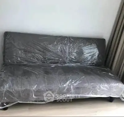 Modern gray sofa wrapped in protective plastic in a stylish living room setting.