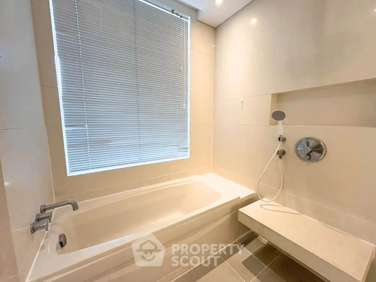 Modern bathroom with sleek bathtub and shower, featuring elegant tile design and natural light.