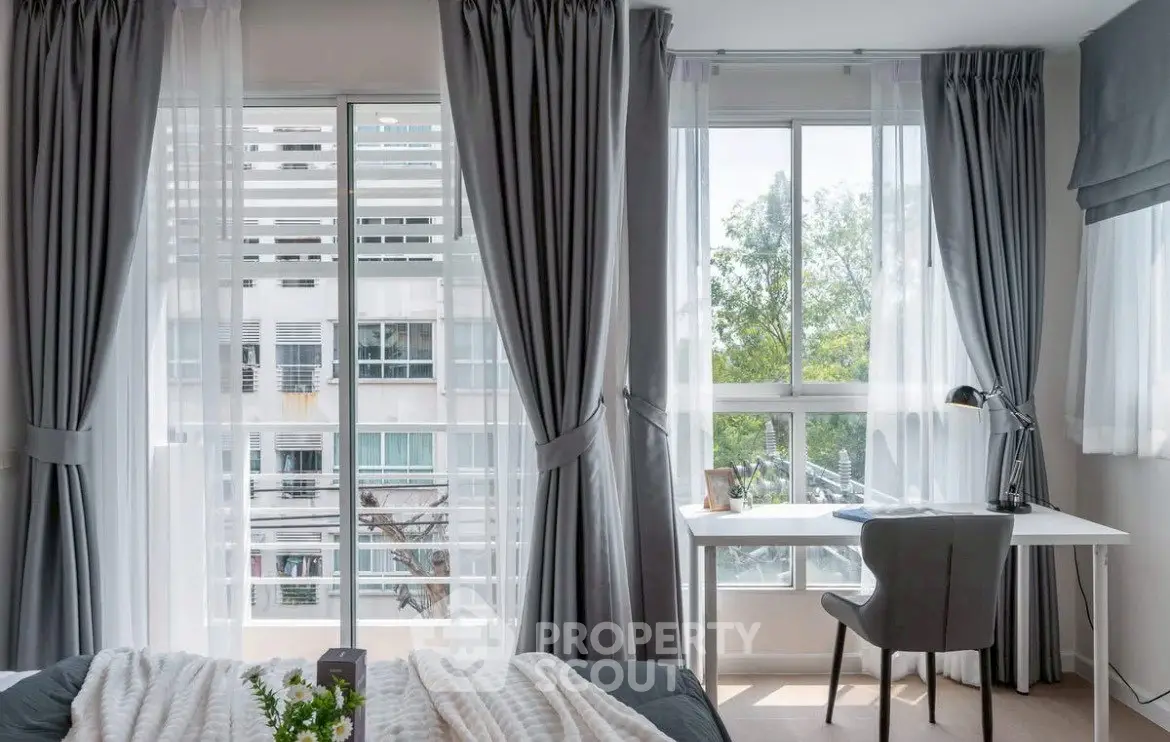 Bright bedroom with large windows and study area, featuring modern decor and natural light.