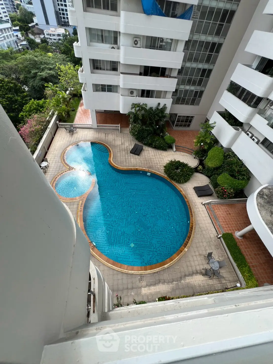 Stunning aerial view of a modern apartment complex with a uniquely shaped swimming pool and lush greenery.