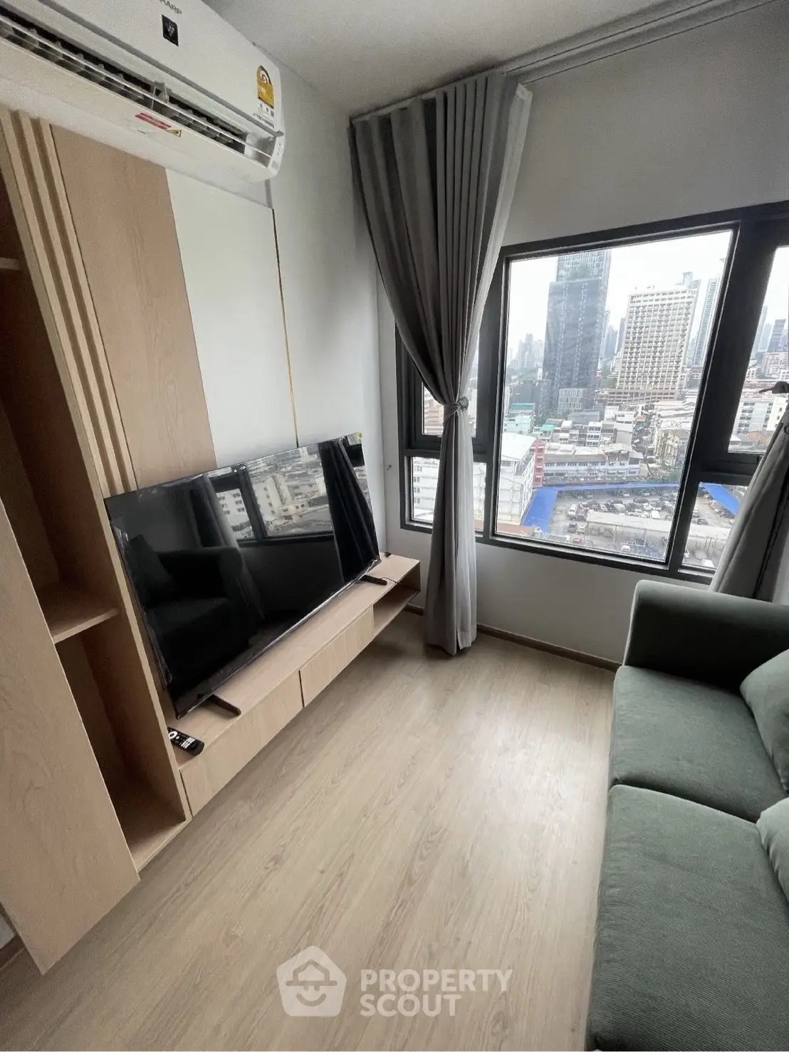 Modern living room with city view, featuring sleek TV setup and large windows for natural light.