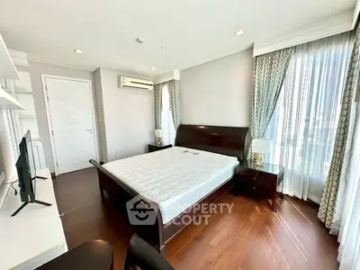 Spacious bedroom with elegant wooden flooring and large windows offering natural light.