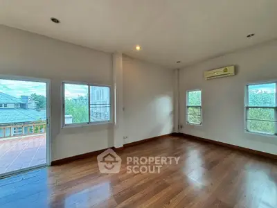 Spacious empty room with wooden flooring and large windows offering natural light and scenic views.