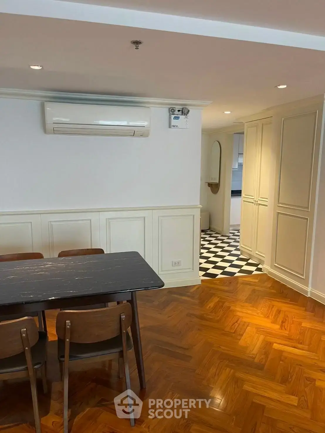 Stylish dining area with parquet flooring and air conditioning, leading to a chic black-and-white tiled hallway.