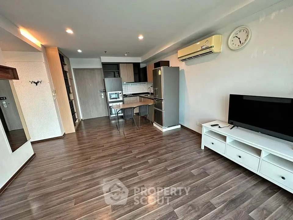 Modern open-plan living room with kitchen, featuring sleek wooden flooring and contemporary furnishings.