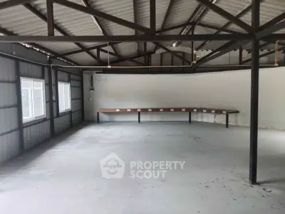 Spacious industrial-style room with exposed beams and large windows, ideal for creative workspace or studio.
